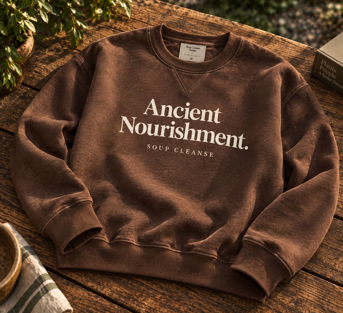 Brown earth-toned sweatshirt reading Ancient Nourishment in serif type, with Soup Cleanse in small type beneath.