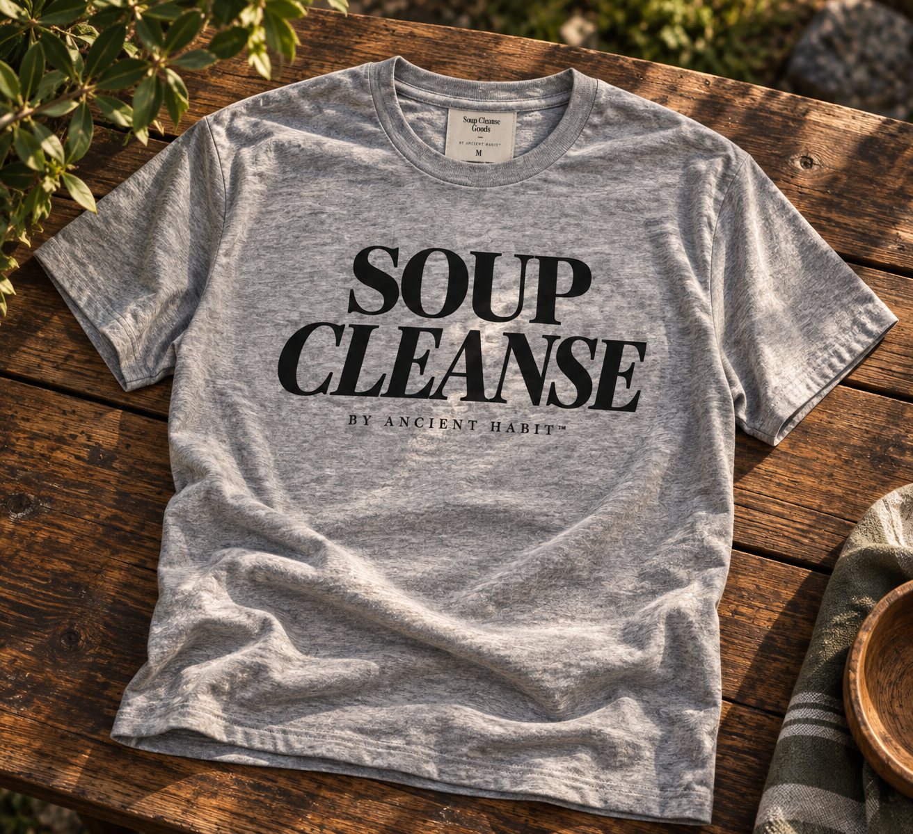Heather grey T-shirt with stacked serif SOUP CLEANSE typography and a small BY ANCIENT HABIT line beneath.